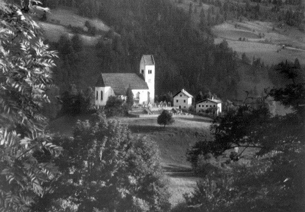 Blick auf St. Georgen im Pinzgau mit Kirche und alten Häusern in einer Berglandschaft.