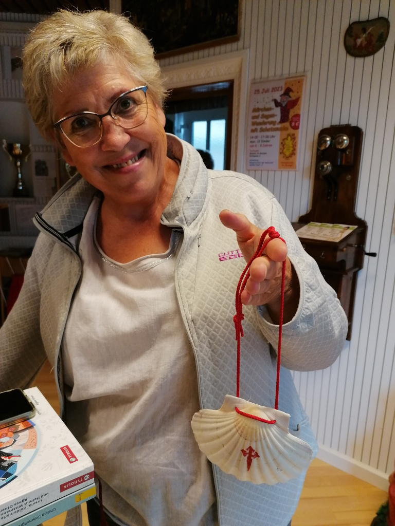 Frau zeigt Jakobsmuschel mit rotem Band