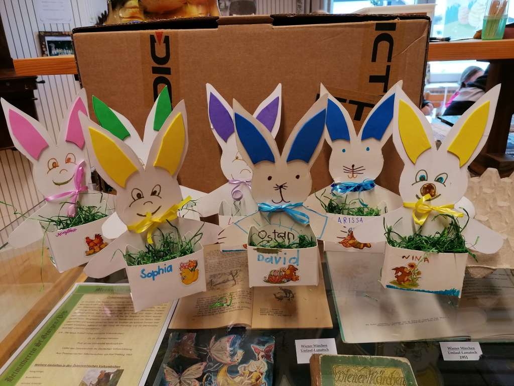 Bunte Papierhasen mit Namensschildern und Ostergras auf einem Tisch